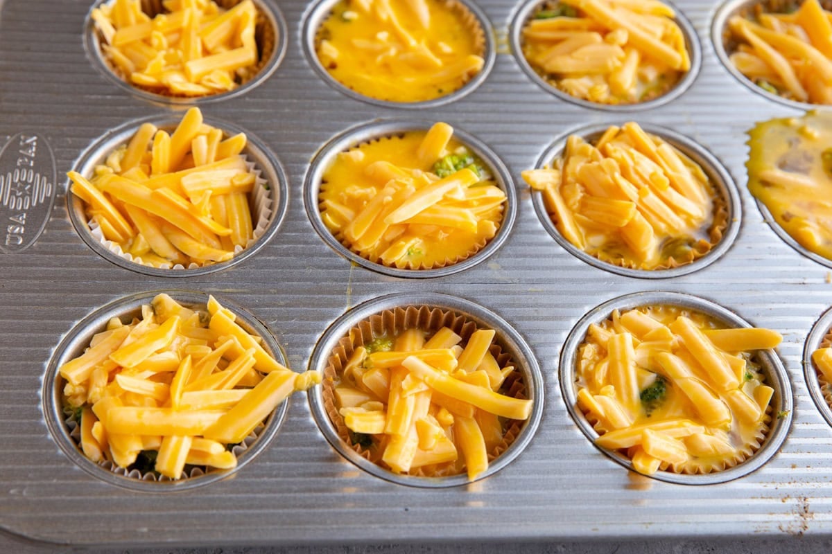 Muffin tin with broccoli, eggs, and cheddar cheese, ready to go into the oven to make egg muffins.