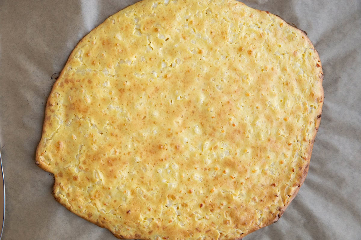 Cottage cheese pizza crust fresh out of the oven on a baking sheet with no toppings on it.
