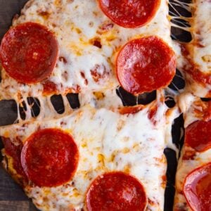 Cottage cheese crust pizza sitting on a wooden cutting board cut into four slices with the slices pulled apart for a cheese pull.