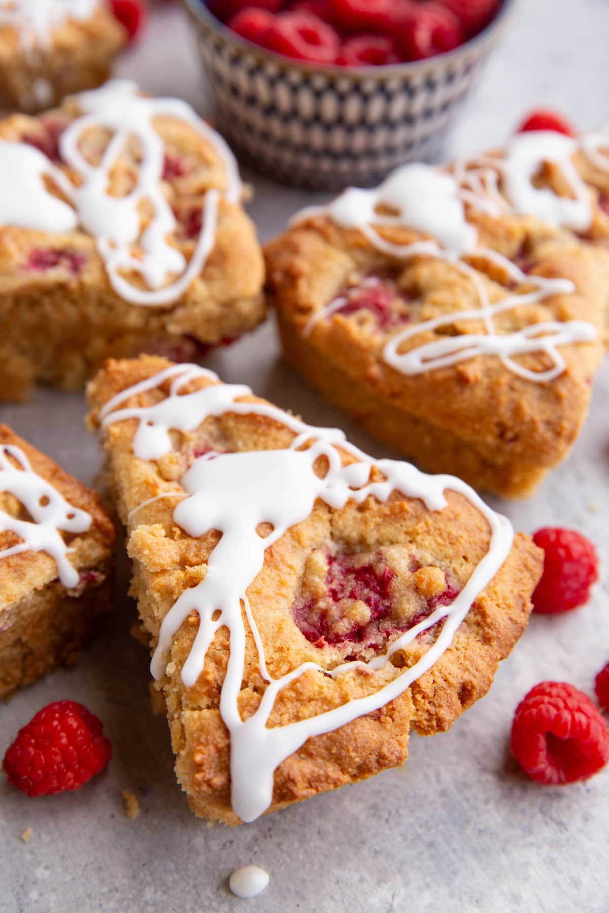 Several raspberry scones drizzled with glaze with fresh raspberries around, ready to serve.