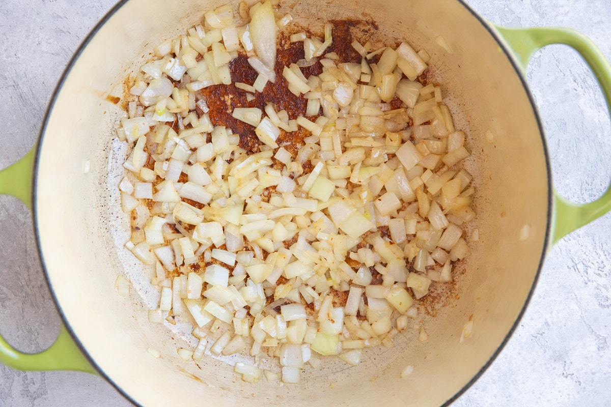 Dutch oven with onions cooking inside bacon fat.