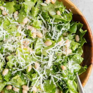 Wooden bowl full of romaine lettuce, parmesan cheese, and white beans dressed with lemon dressing.