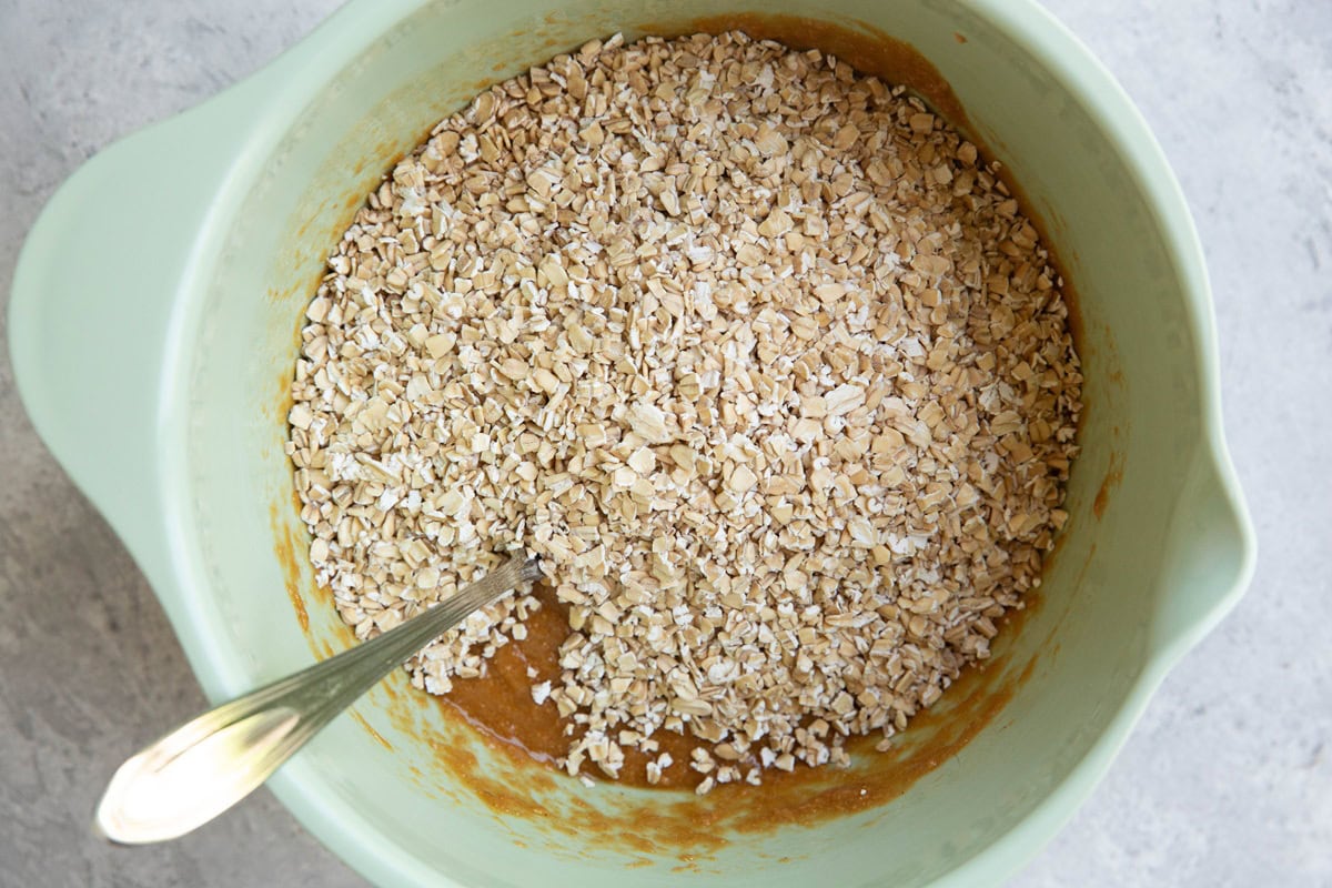 Pale green mixing bowl with wet ingredients on the bottom and oats on top, ready to be mixed in.