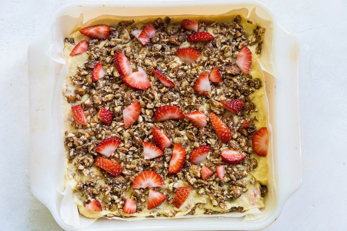 Cake pan with cake batter and streusel topping with chopped strawberries on top.