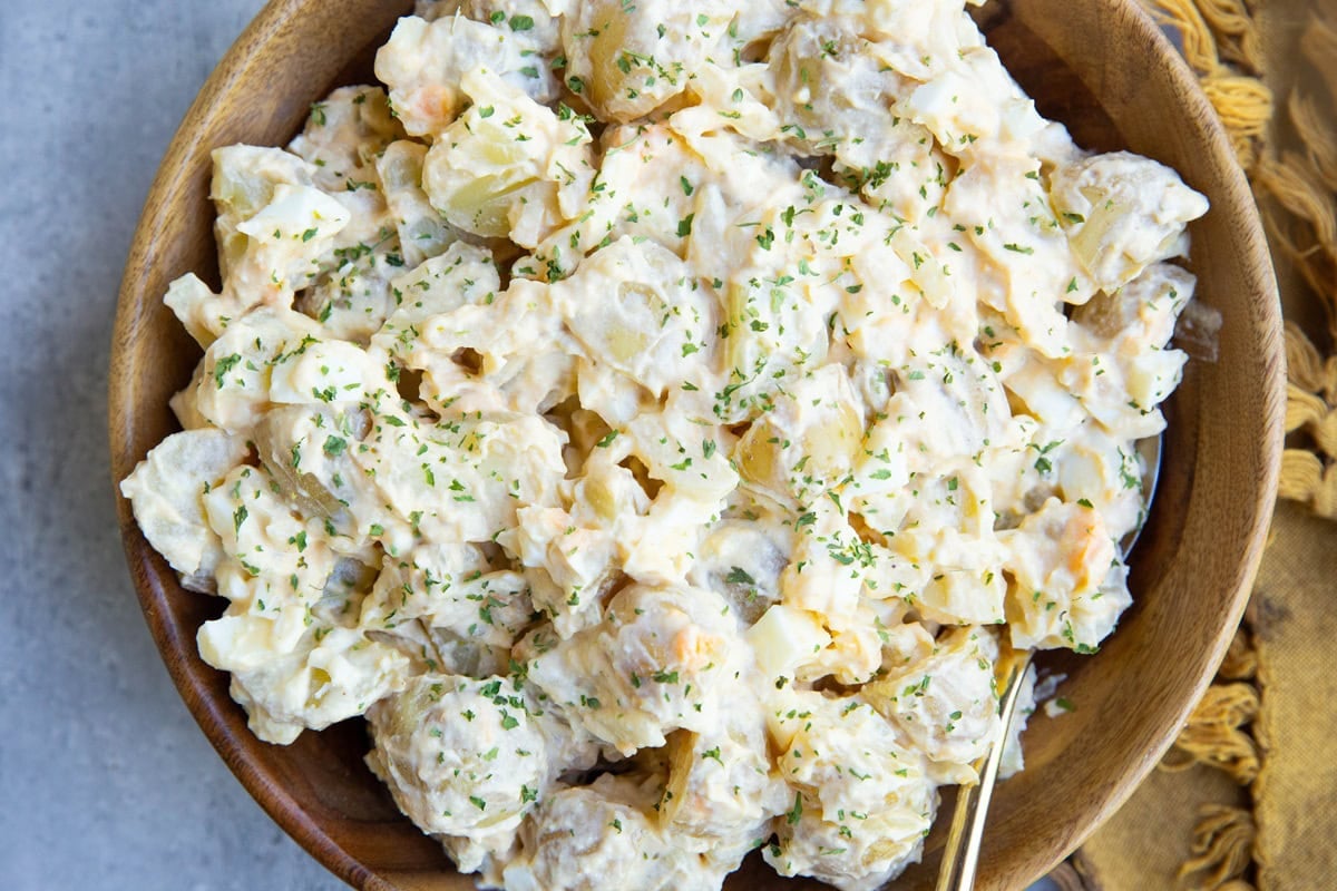 Cottage cheese potato salad in a wooden bowl with a golden napkin to the side.