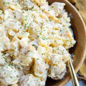 Cottage cheese potato salad in a large wooden bowl with a gold spoon and a gold napkin to the side.