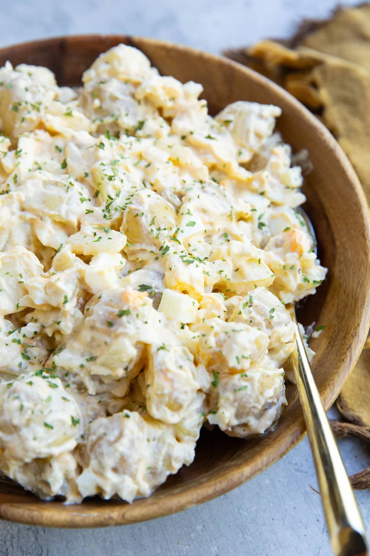 Cottage cheese potato salad in a large wooden bowl with a gold spoon and a gold napkin to the side.