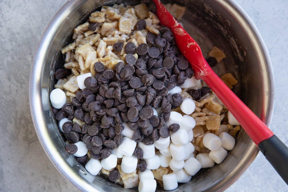 Saucepan with marshmallow coated cereal on the bottom and mini marshmallows and chocolate chips on top.