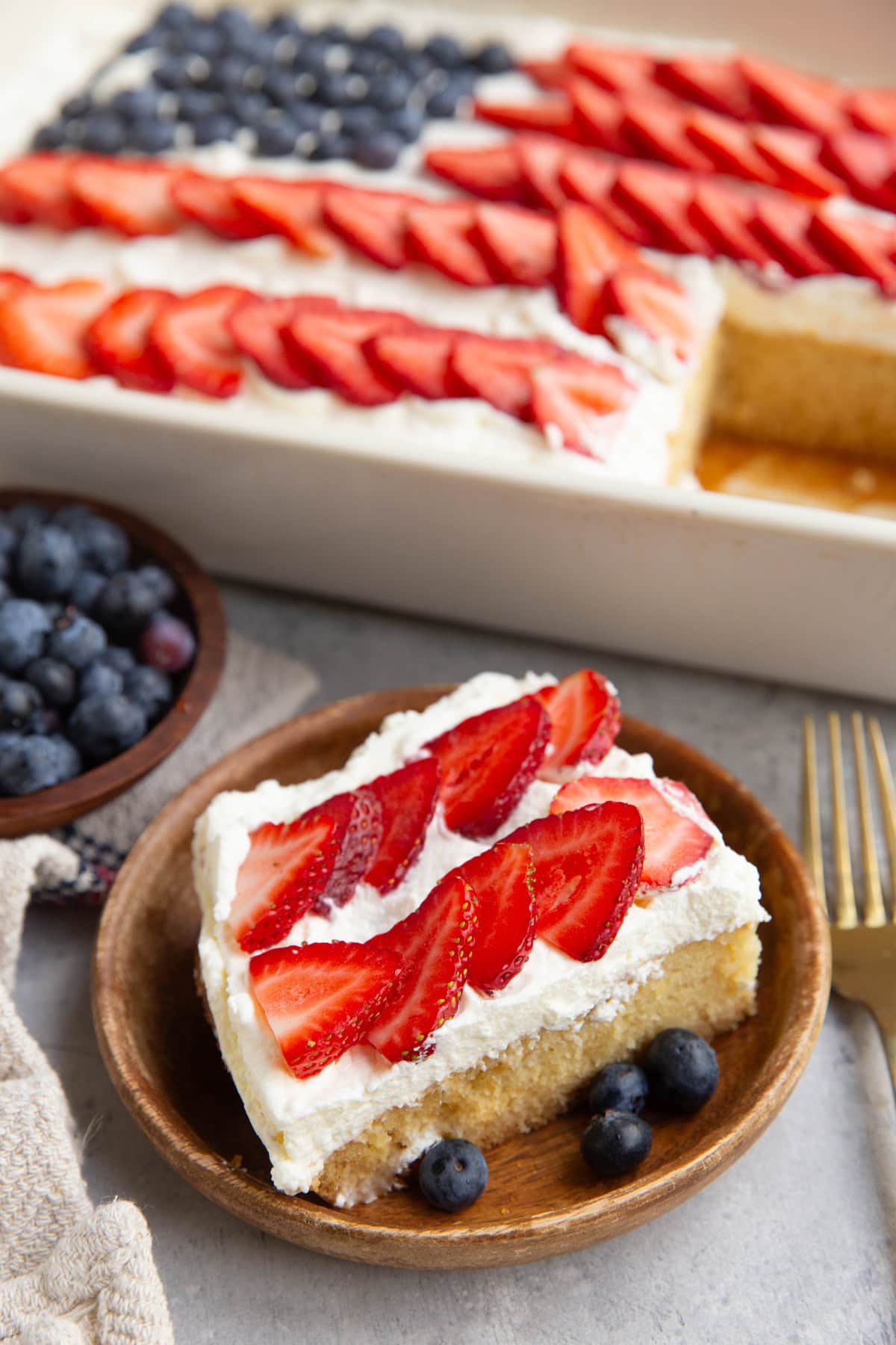 Slice of flag cake on a wooden plate with the rest of the cake in the background.