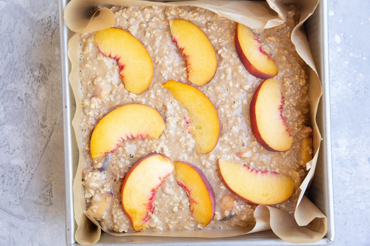 Baking pan with peach oatmeal and sliced peaches on top, ready to go into the oven.