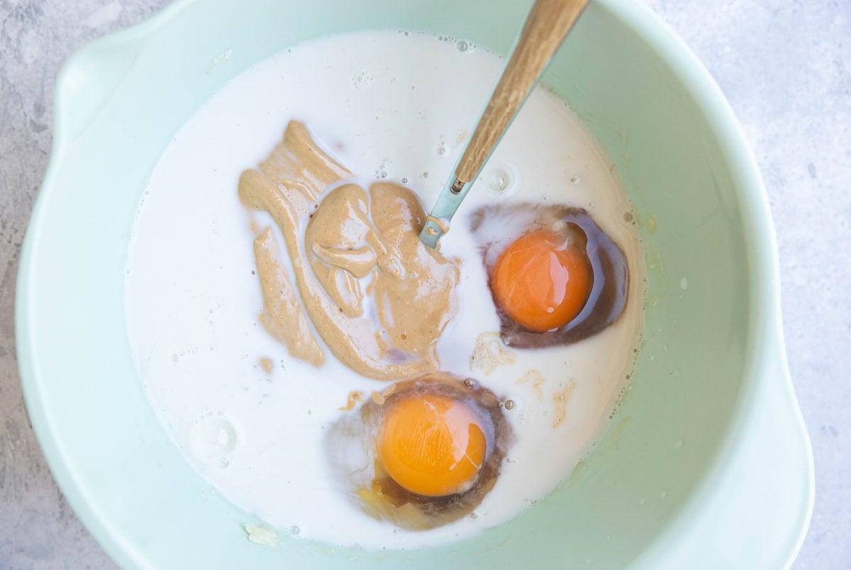 Milk, cashew butter, mashed banana and eggs in a mixing bowl to make baked peach oatmeal.