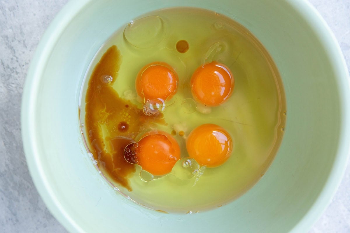 large bowl full of eggs, almond extract, vanilla extract and oil.