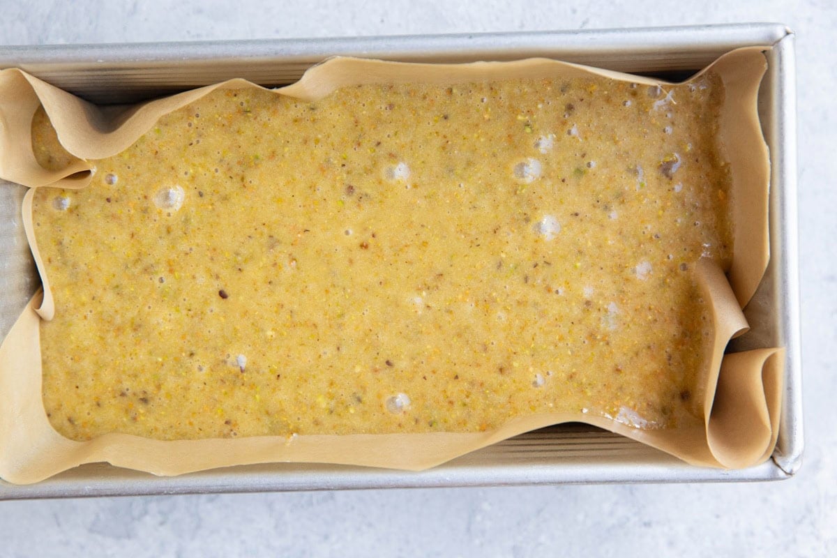 Pistachio cake batter in a loaf pan lined in parchment paper.