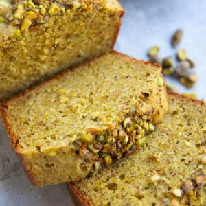 Thick slices of pistachio cake with raw pistachios in the background. The slices are in the form of a loaf.