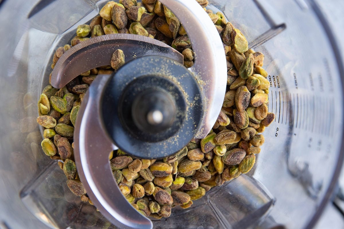 Food processor with raw pistachios inside, ready to be pulsed into pistachio flour.