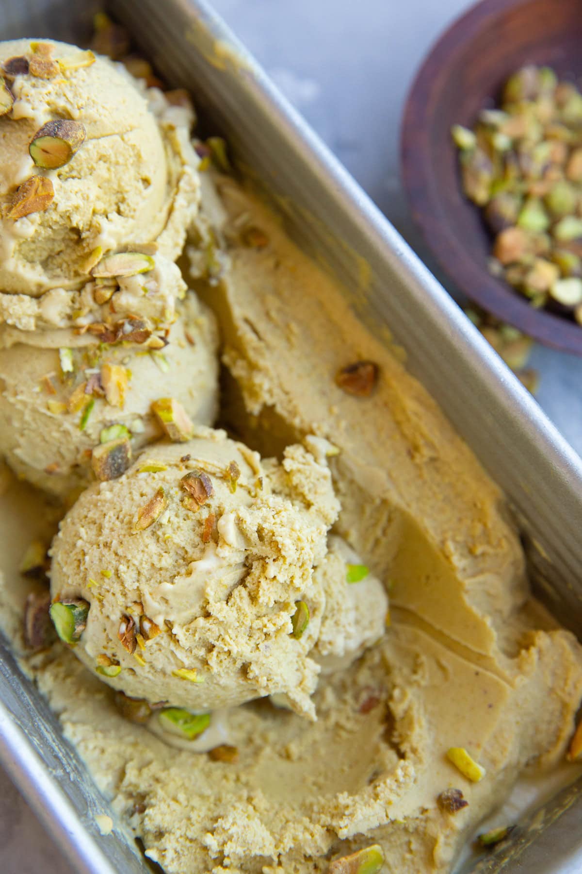 Pistachio ice cream in a loaf pan with a bowl of pistachios to the side.