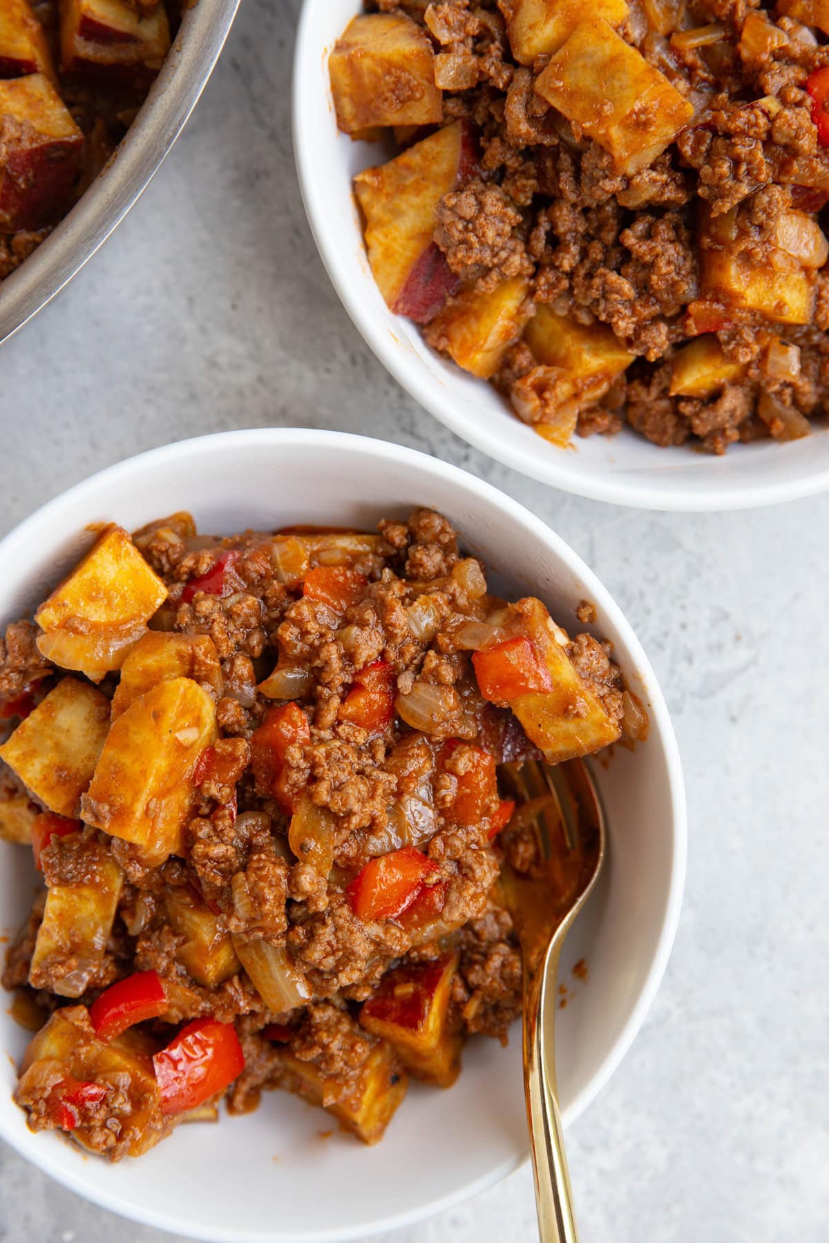 Two white bowls of sweet potato sloppy joes with the skillet with the rest of the recipe to the side.