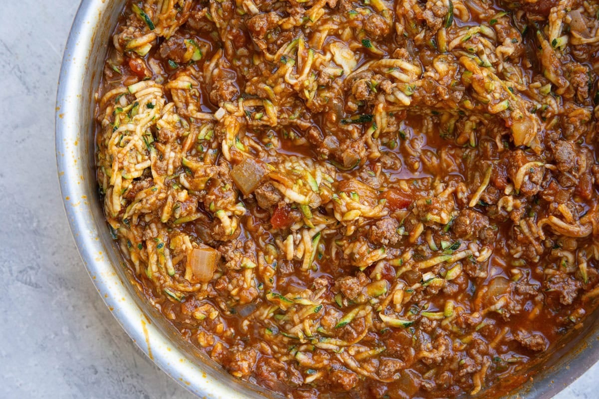 Stainless steel skillet full of meat sauce and grated zucchini.