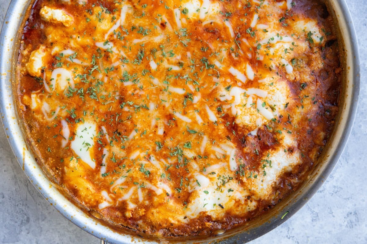 Stainless steel skillet with zucchini lasagna inside, with melted cheese and dried parsley on top. Ready to serve.