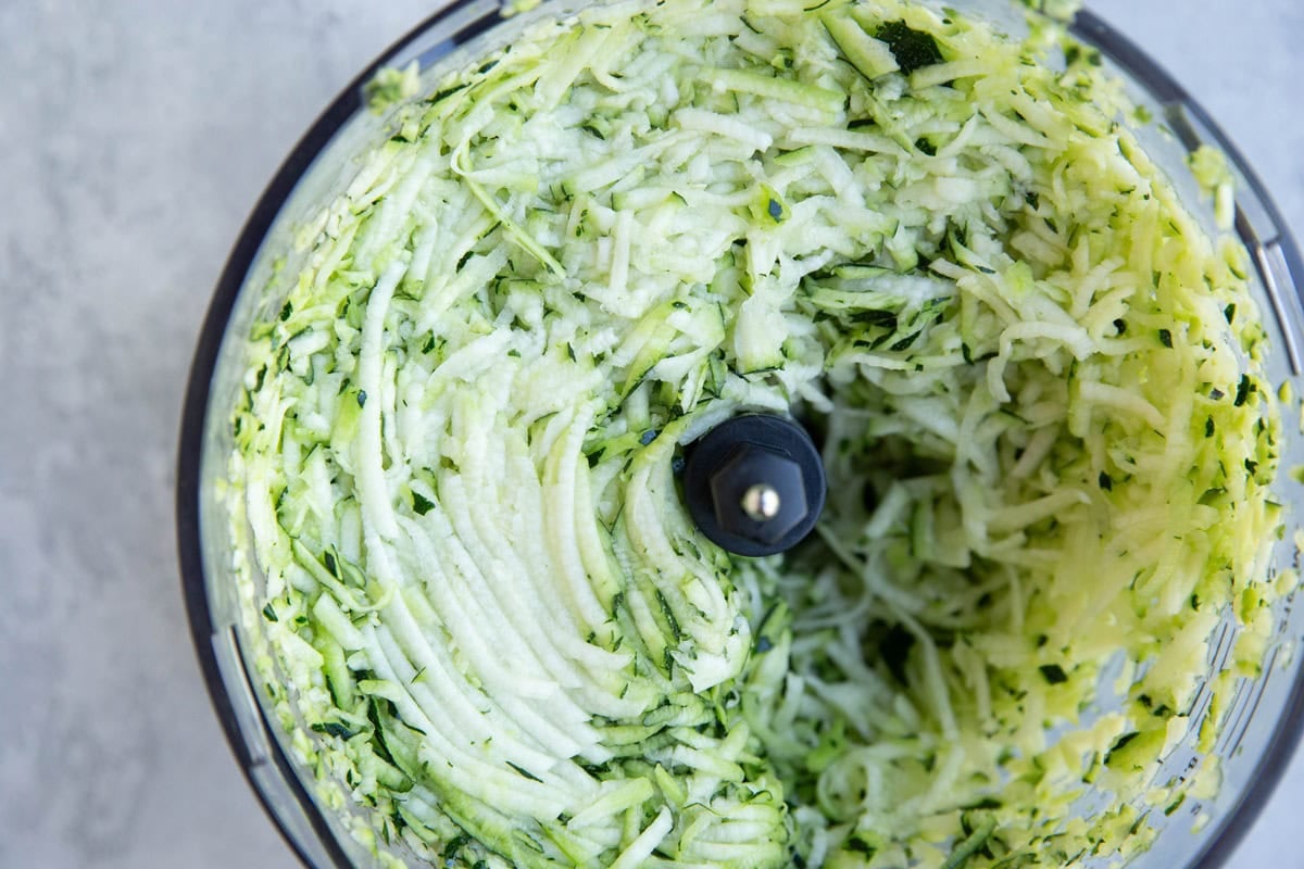 Food processor filled with grated zucchini.